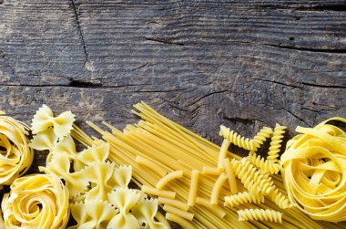 Çeşitli türleri ve İtalyan makarna yukarıdan eski ahşap arka plan üzerine şekiller. İtalyan mutfağı gıda kavramı ve menü tasarımı. Kuru makarna arka plan. Üstten görünüm. Düz yatıyordu. Kopya alanı.