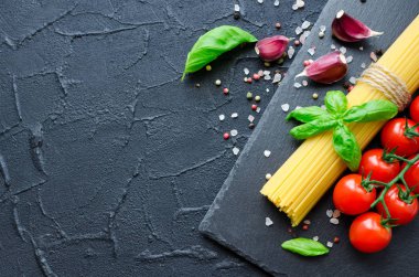 İtalyan pasta - yemek pişirmek için malzemeler spagetti, domates, fesleğen ve sarımsak metniniz için yer ile koyu arka plan üzerinde kayrak gemide. İtalyan mutfağı kavramı. Uzay kopyalayın. Üstten görünüm.