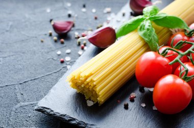 İtalyan pasta - yemek pişirmek için malzemeler spagetti, domates, fesleğen ve sarımsak koyu arka plan üzerinde kayrak gemide. İtalyan mutfağı kavramı.
