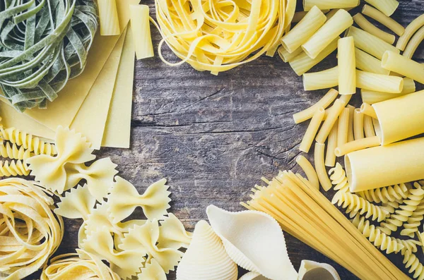 Frame from variety of types and shapes of Italian pasta on old wooden background from above. Italian cuisine food concept and menu design. Dry pasta background. Top view. Flat lay. Copy space.