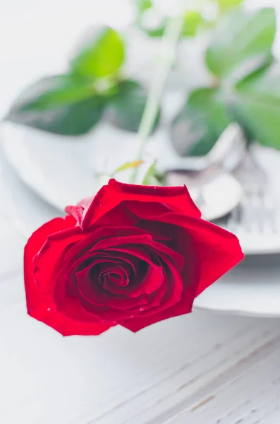 Close up view of restaurant table with romantic place setting with red rose, plates, cutlery on white background. Valentine\'s Day or romantic dinner concept. Valentine day or proposal background.