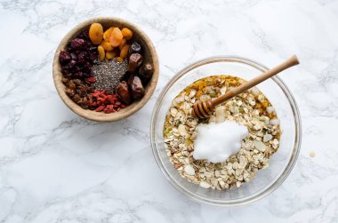 Ev yapımı granola hazırlık süreci. Agav nektarı, hindistan cevizi yağı ve kurutulmuş meyve, çilek ve chia tohumları sonra eklemek ile cam kase de pişirme için karışık malzemeler. Superfood. Üst te. Düz yatıyordu.