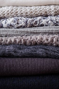 Yünlü yün kazak yığını. Monokrom eğimli gölgeler gri beyaz siyah renkler farklı örgü desenleri yığılmış giysiler. Sıcak kış kış sonbahar örgü konsepti. Boşluğu kopyala.