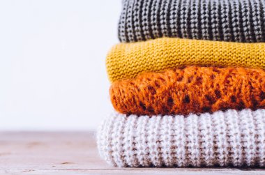 Ahşap masa üzerinde örme yünlü kazak sonbahar renkleri kazık. Farklı örgü desenleri ile giysi yığını katlanmış. Sıcak rahat kış sonbahar triko kavramı. Kopyalama alanı.