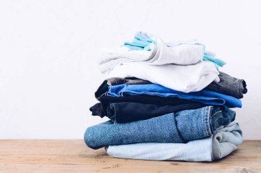 Masanın üstündeki giysi yığını. Ev konsepti. Taze katlanmış pamuk kot giyim. Ütü, bağış, ev işi konsepti.