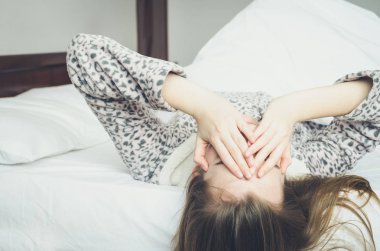 Güneşli sabah mutlu genç kadının. Beyaz kız yatakta uzanan ve uyanma sonra gülümseyen sevimli sıcak pijama. Gün kavramının iyi başlangıç.
