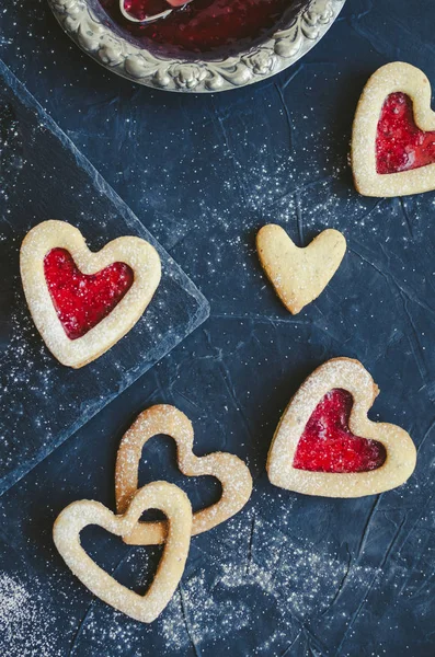 Heart shaped Linzer cookies with jam for Valentine\'s day on black background. Delicious homemade pastry. Baking with love concept. Top view.