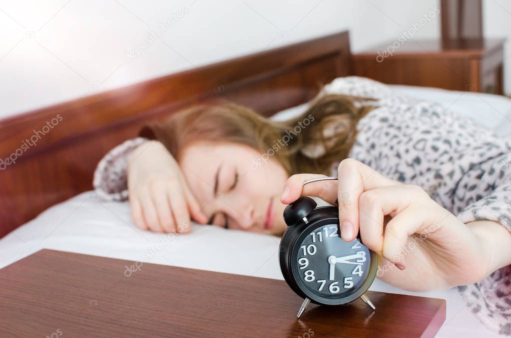 Young woman girl turns off alarm clock waking up in the morning from a call. Schoolgirl or student do not want to wake up early for school or univercity. Oversleep, not getting enough sleep concept.