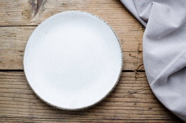 Beyaz tabak ve ahşap zemin üzerinde gri keten peçete, yazı için yer var. Yemek arkaplanı. Güzel anlaşma. Menü modeli. Düz yatıyordu. Üst Manzara. Boşluğu kopyala.