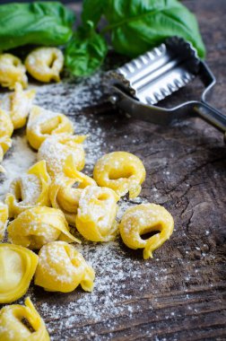 Taze ev yapımı ham flouring tortellini fesleğen yaprakları ile ahşap vintage kesme tahtası üzerinde pişirmek hazır hazır. Geleneksel İtalyan mutfağı kavramı. Seçici odak.