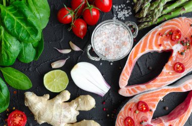 İki taze Çiğ somon biftek sebze ve baharatlar ile: kuşkonmaz, ıspanak, sarımsak, domates, zencefil, biber, tuz, biber, soğan ve siyah arka plan üzerine limon. Sağlıklı gıda diyet kavramı. Üstten Görünüm.