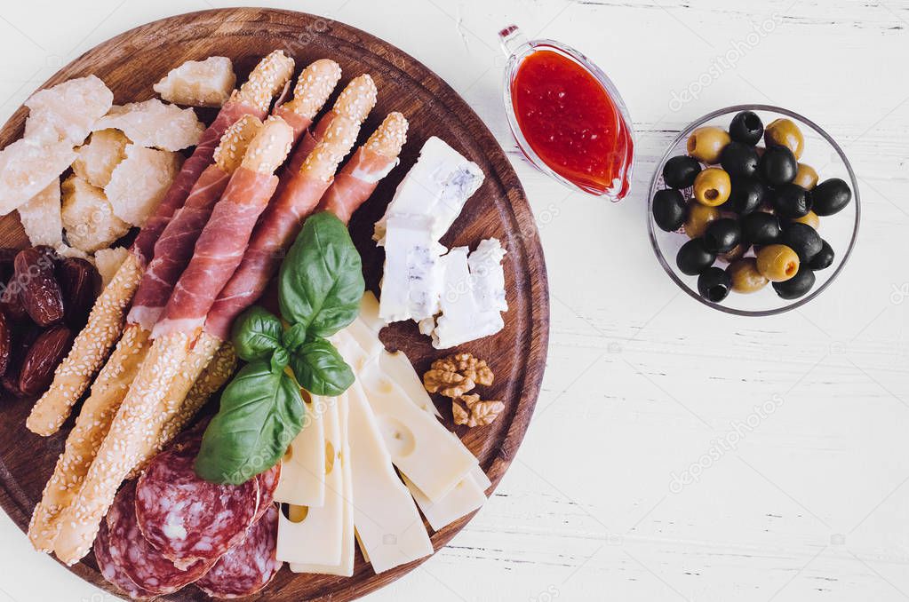 Wooden board full of mediterranean appetizers, tapas or antipasti. Assorted Italian style banquet food set. Delicious snack on party. Chopping board with meat and cheese. Top view. Copy space.