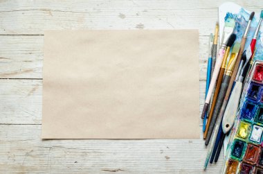Sanatçı boya fırçaları ve ahşap zemin üzerinde suluboya boya boya kutuları ve boş kağıt yaprakları. Yaratıcı eğlence için aletler ve aletler. Resim sanatı konsepti modeli. Üst Manzara. Uzayı kopyala Düz yatıyordu.