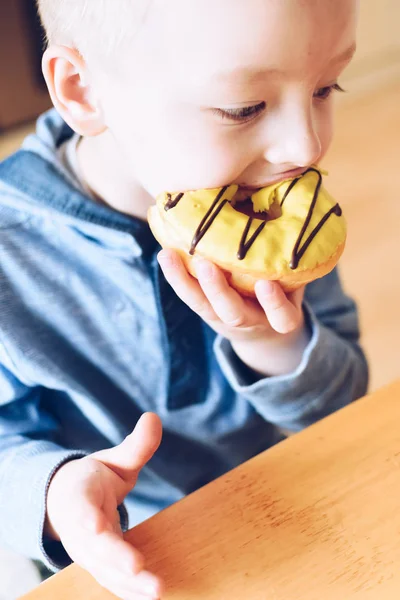 O miúdo está a comer donut. — Fotografia de Stock