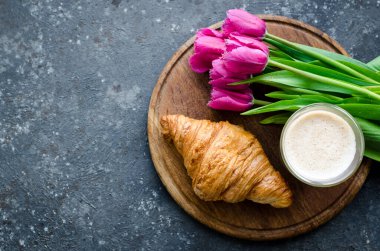 Bir fincan kahve, pembe laleler ve siyah arka planda kruvasan. Sevgililer Günü, Anneler, Kadınlar Günü sabahı konsepti. Sevgililer Günü kahvaltısı. Üst Manzara. Boşluğu kopyala.