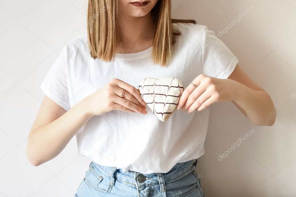 Female hand holding heart shaped donut with white glaze and chocolate hearts rhythm decoration. Love, romantic, Valentines day concept.