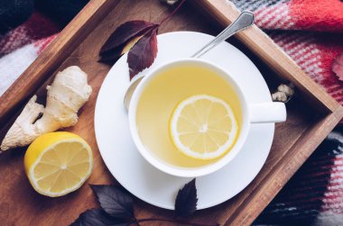 Sıcak, yeşil çay, zencefil ve limonlu ahşap tepside sonbahar yaprakları kırmızı, sıcak, yün battaniyeye dökülmüş. Soğuk havada dinleniyor. Gribe karşı doğal ilaçlar. Mevsimlik içecekler. Üst görünüm.