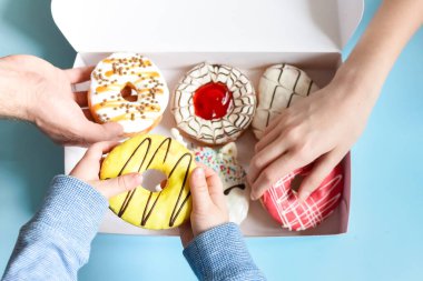 İnsanlar donut kutusundan donutları mavi arka plandan alıyor. Yemek dağıtımından aile donutları yiyor. Sağlıksız yaşam tarzı kavramı. Üst görünüm veya düz uzanma.