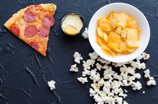 Fast food and unhealthy eating concept. Close up of fastfood snacks: pizza, popcorn and potato chips. Assortment of carbohydrates products bad for figure, skin, heart and teeth. Top view.