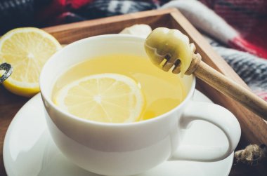 Sağlıklı yeşil çay, zencefil, bal ve limon ile ahşap tepside, sonbahar yaprakları sıcak yün battaniyeye dökülmüş. Soğuk havada dinleniyor. Gribe karşı doğal ilaçlar. Mevsimlik içecekler.