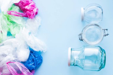 Birçok tek kullanımlık plastik torba mavi arka planda yeniden kullanılabilir cam kavanozlara karşı. Sıfır atık. Sürdürülebilir yaşam, plastiksiz konsept. Eko dostu plastik eşyalar. Üst görünüm.