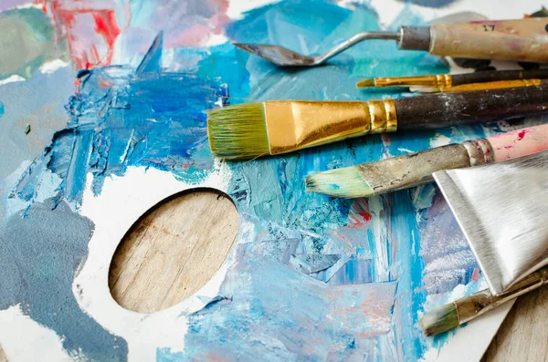 画家在木制调色板上刷子和油漆管 纹理混合油画在不同的颜色和饱和度 创造性闲暇的工具和手段 绘画业余爱好 回学校去 — 图库照片