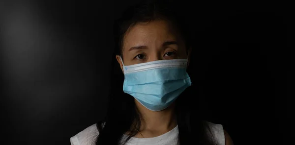 Woman wearing protection face mask against coronavirus or COVID-19 in darken tone. Banner with copyspace for medical concept