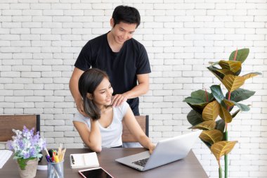 Evde dizüstü bilgisayarla çalışan genç ve gülümseyen bir çiftin portresi rahatlatan bir kızın omuzuna masaj yapmak.