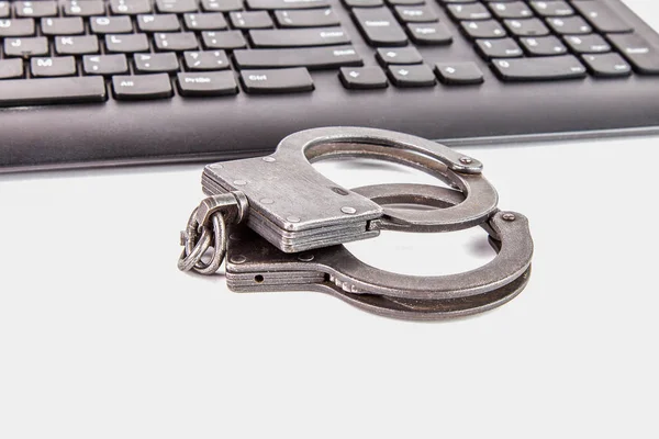 Police handcuffs lying on a dark computer keyboard