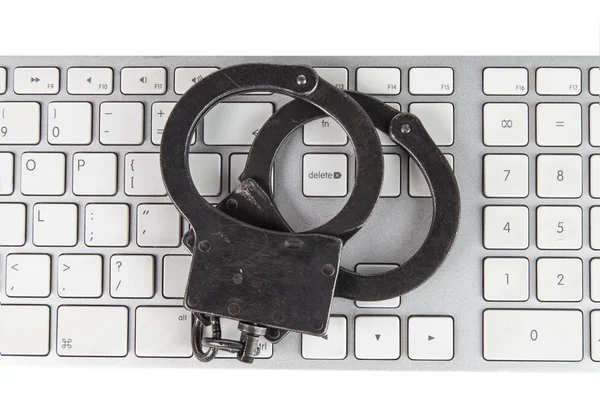 Police handcuffs lying on a light computer keyboard