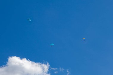Beyaz bulutlarla mavi gökyüzünün arka planında üç yamaç paraşütü