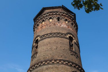 Mavi gökyüzüne karşı farklı boyutlarda pencereleri olan eski kırmızı tuğla kule