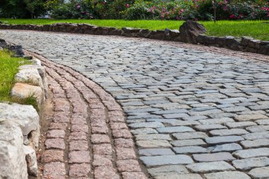 Taş döşeli bir yol. Bitkilerin çiçekli çalılar arka planda görülebilir.