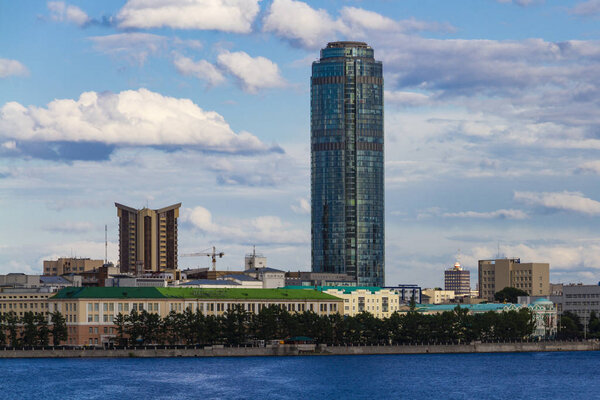 City landscape - a skyscraper towering above the surrounding buildings against the cloudy sky. In the foreground is a lake