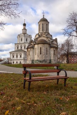 Bulutlu gökyüzünün arka planında antik ortodoks taş tapınağı. Ön planda bir bahçe bankı var..
