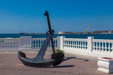 Beyaz taştan bir çitin ve mavi denizin arka planına karşı setin üzerinde büyük bir karabatak uzanır.