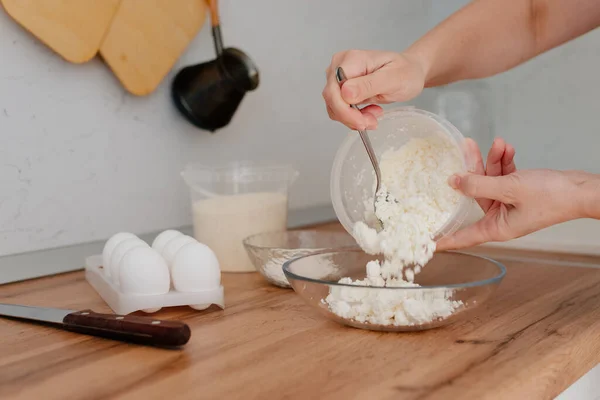 Peynirli krep. Ev mutfağında cheesecake yapma süreci. Bir kase süzme peynir, bir kadın süzme peyniri bir kaseye dolduruyor ve yumurta sürüyor. Süzme peynir ve yumurta sarısı.