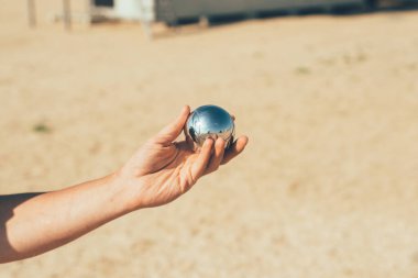 Playing boccia on the beach. A man holds a boccia ball in his hand. Shiny chrome petanque ball with reflections. clipart