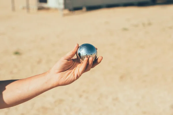 Kumsalda Boccia oynuyorum. Adamın biri elinde bir boccia topu tutuyor. Yansımalı parlak krom petank top.