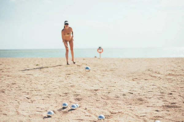 Playing boccia on the beach. The girl throws a shiny silver ball into the sand. Image of girl playing petanque on sand on holidays.