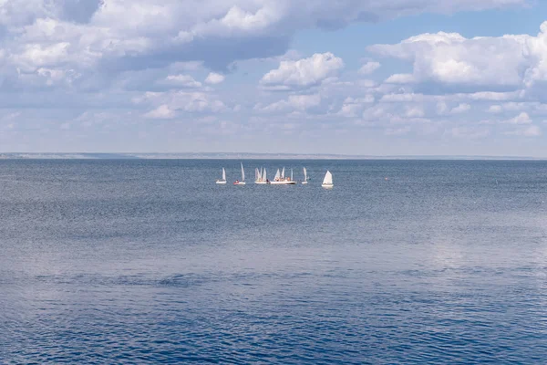 Small yachts with white sails in the middle of the sea. Blue sea, and above it the sky with clouds. Yachting team coaching.