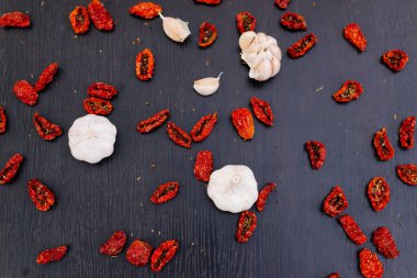 Kurutulmuş domates, sarımsak ve baharatlar siyah ahşap bir zemine saçılmıştır. Domates dokusu