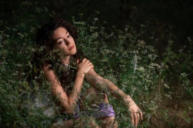 Güzel genç bir kadın karanlık bir ormanda poz veriyor. 