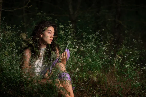 Güzel genç bir kadın karanlık bir ormanda poz veriyor. 