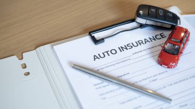 Auto insurance document with car key pen and red car model on wooden desk representing vehicle protection accident claim financial security safety assurance and legal coverage