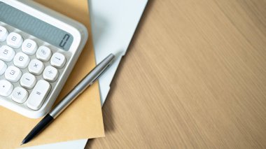 Hesap makinesi kalem ve kahverengi klasör ahşap masa üzerinde güneş ışığı temsil eden ofis işi kredi planlama ipotek sigortası tasarruf planı finansal strateji yatırım yatırım uzun vadeli varlık yönetimi.