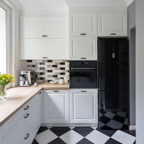 Small, white kitchen with modern chess flooring and black fridge