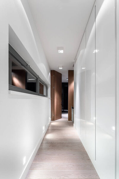 White and elegant home corridor with wardrobe, small window and wooden floor