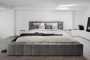 Beyaz duvarları, gri zemini ve tavan penceresi olan büyük, gri ve yorgan kaplı yatak odası.