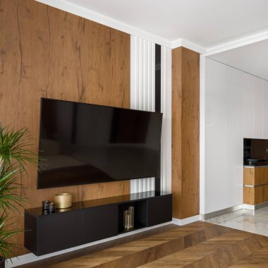 Oturma odasında ahşap duvarları, ahşap zemini ve beyaz pervazı olan büyük bir televizyon ekranı.